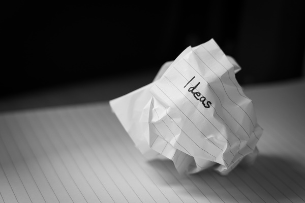 Image description – a photo of scrunched up piece of lined paper with ‘ideas’ written in black ink is shown on top of a lined notepad with a black background